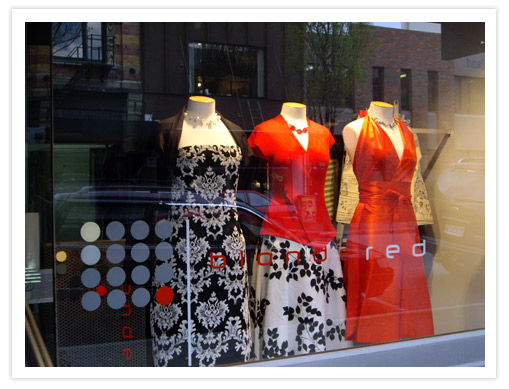 A display window of the Blond Red fashion boutique on High Street featuring a variety of dresses, including a striking red dress, set against a stylish backdrop.