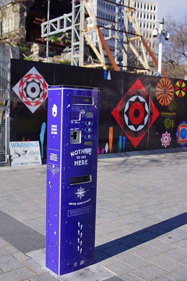 A purple parking meter with the text 'NOTHING TO SEE HERE' is displayed in Cathedral Square, surrounded by a colorful mural and construction site.