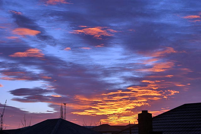 A vibrant sunrise with colorful clouds illuminates the sky above rooftops.