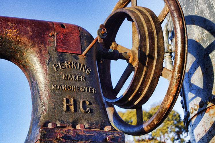 Close-up of an old, rusty machine part with the inscription 'Perkins Maker Manchester' and a circular wheel, resembling a steampunk design.