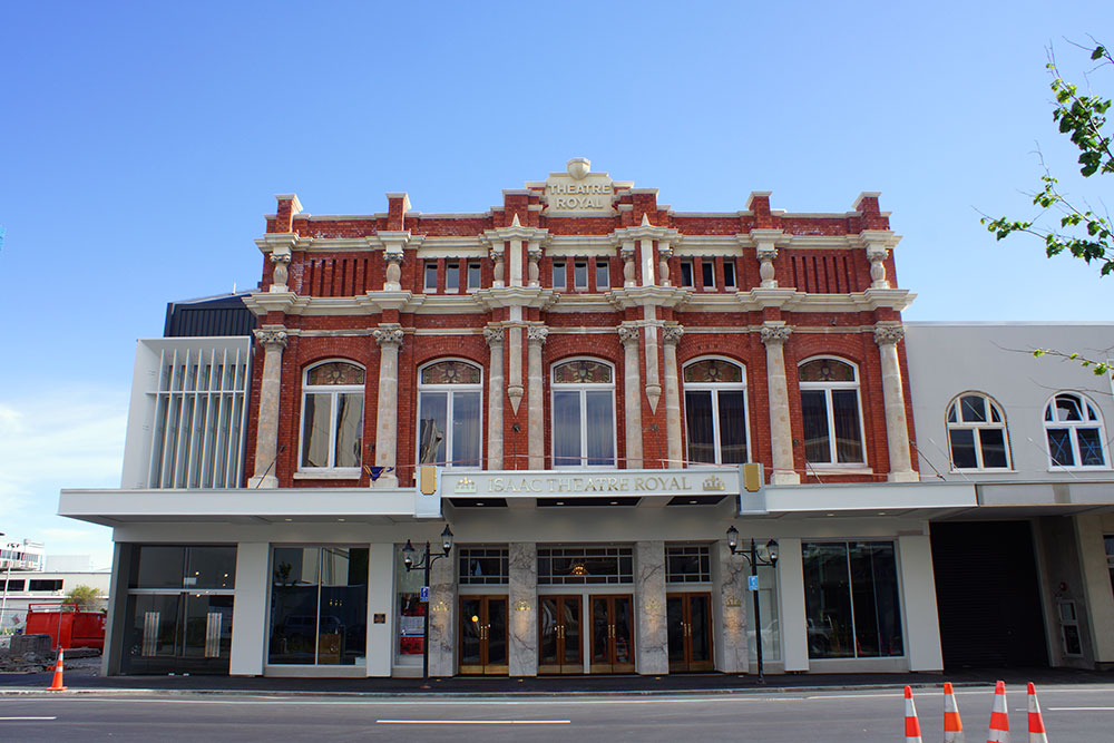 The front façade of the Isaac Theatre Royal, showcasing its historic architecture with a blend of red bricks and decorative features under a clear blue sky.