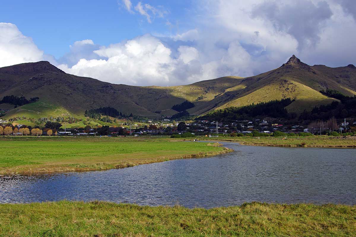 A scenic view of Castle Rock and surrounding hills under cloudy skies, with a river and green fields in the foreground.