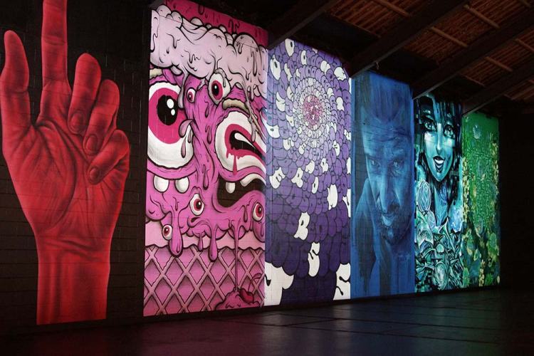 A colorful mural featuring various street art styles, including a red hand gesture, vibrant characters, and abstract designs, displayed on the walls of an indoor venue.