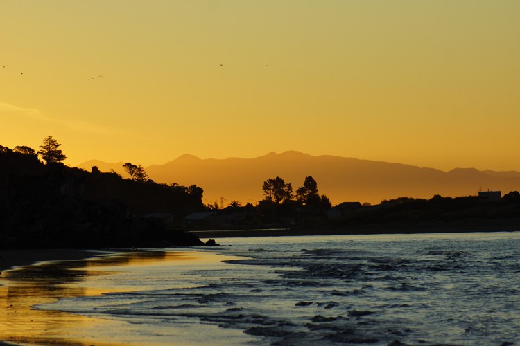 Sunset over Sumner Beach with silhouettes of mountains and trees reflected in the water.