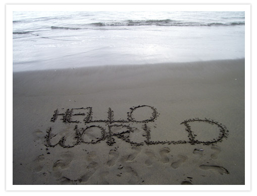 The words 'HELLO WORLD' written in sand on a beach, with gentle waves in the background.