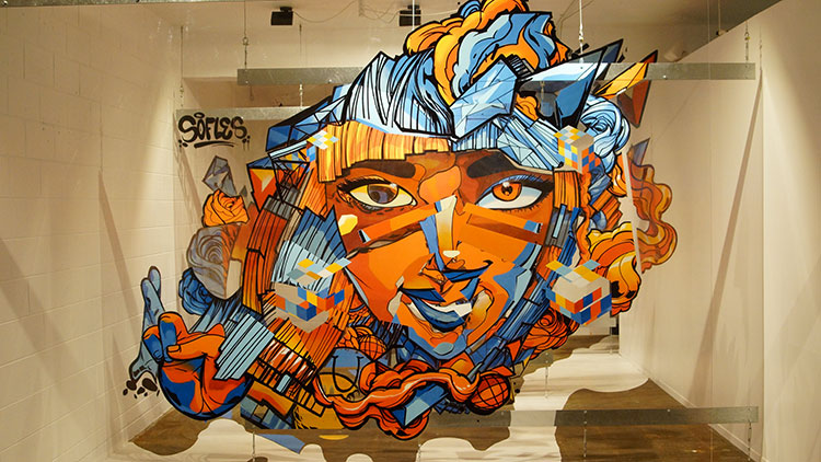 A vibrant street art mural featuring an abstract face with colorful geometric shapes and flowing lines.