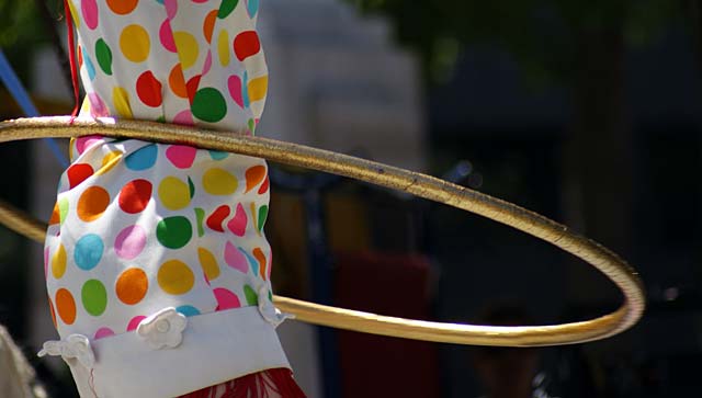 A performer at the Busker's festival twirls a hula hoop while wearing a colorful polka dot outfit.